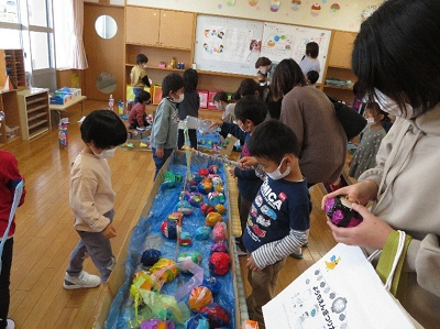 室内の遊びコーナーで子供たちがカラフルなボール遊びを囲んで楽しんでいる写真