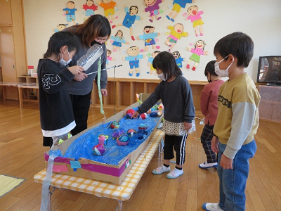 室内の遊びコーナーで子供たちが手作りの水遊びスペースでボール遊びをしている写真