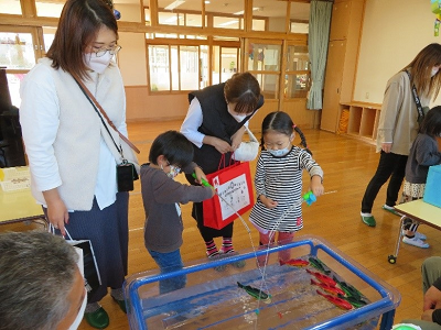 室内の水遊びコーナーで保護者に見守られながら子供たちが魚つり遊びをしている写真