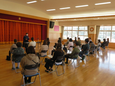 遊戯室で職員の説明を保護者が椅子に座って聞いている写真