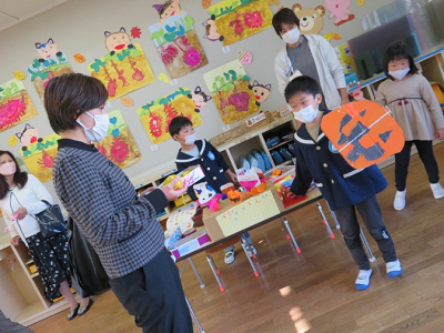教室で先生が園児にハロウィーンの制作物を手渡している写真