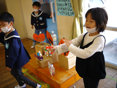 教室の窓際で女の子がハロウィーンの飾りを両手に持って見せている写真