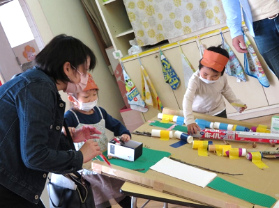 室内で先生が園児の工作を隣で手伝っている写真