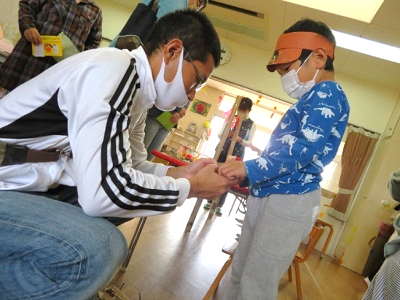 室内で保護者が園児の仮装の目隠しやお面を身につけるのを手伝っている写真