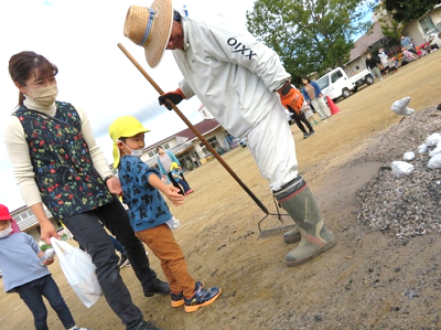 園庭で職員が火床の準備をしながら園児と保護者が見守っている写真