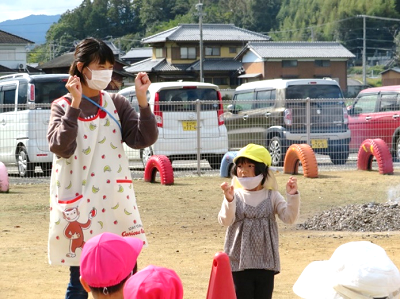 園庭で先生と園児が手遊びのまねっこをしている写真