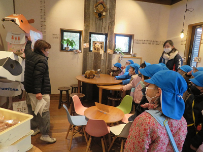 店内で青い帽子の園児達が店員の説明を聞いている写真