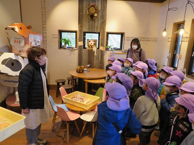 店内でピンクの帽子の園児達が店員の説明を聞いている写真