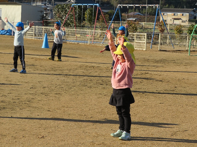 園庭でピンクの服の園児が両手を上げて体操をしている写真