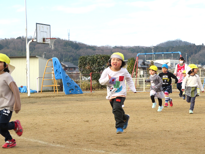 園庭で黄色い帽子の園児たちが並んでマラソンをしている写真