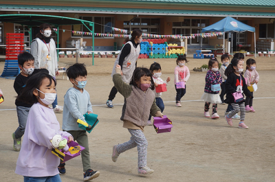 園庭で園児たちが各々紙でできた袋に前も入れて、力いっぱい豆をまいている写真