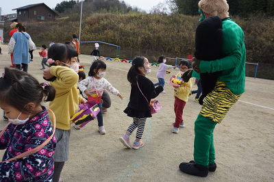 緑の鬼と戯れながら豆まきを楽しんでいる園児たちの写真