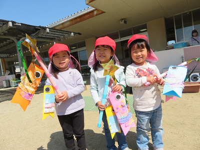 赤い帽子を被った3人の女の子が笑顔でカラフルな手作りのこいのぼりを片手に持っている写真