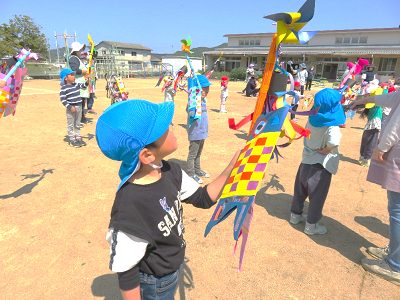 水色の帽子を被った男の子が風にたなびく手作りこいのぼりを見つめている写真