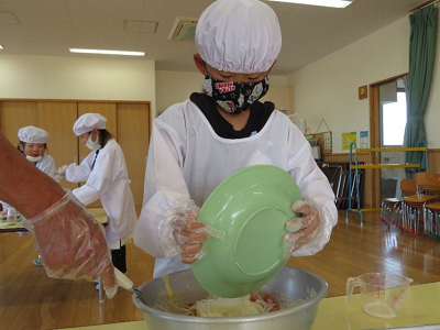 給食用の白衣を着てアルミのボウルに具材を入れている男の子の写真