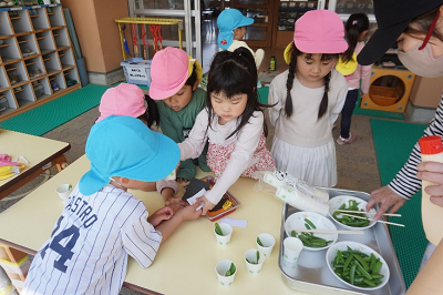 茹でた鮮やかな緑色のスナップエンドウを食べる園児たちの写真