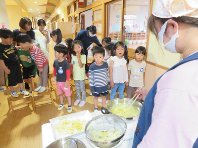 先生がポテトチップスを茹でている様子を興味津々に見つめている園児たちの写真