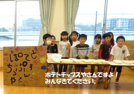 「ぽてとちっぷすやさん」と書かれた手作りの看板の近くのテーブルに沢山のポテトチップスが並べられ、その前に園児たちが並んでいる写真