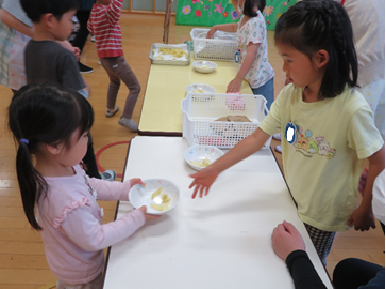 黄緑色のシャツを着た女の子が手渡したポテトチップスが入ったお皿を受け取っているピンクのシャツの女の子の写真