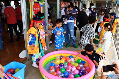 色とりどりのカラフルなヨーヨーが入ったビニールプールでヨーヨー釣りを楽しんでいる園児たちの写真