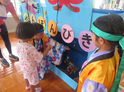 ピンクの浴衣を着た女の子が黄色い法被を着た男の子に教えてもらいながらお菓子つりをしている写真