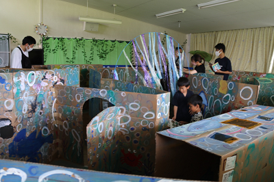 様々な海の生き物が描かれた段ボールが迷路状に並べられたすいぞくかんめいろを楽しむ園児たちの写真