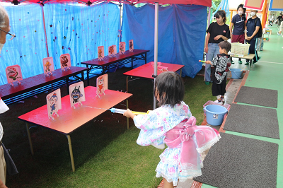 ばいきんまんやドキンちゃんが描かれた紙の的に水鉄砲でまとあてを楽しんでいる女の子の写真