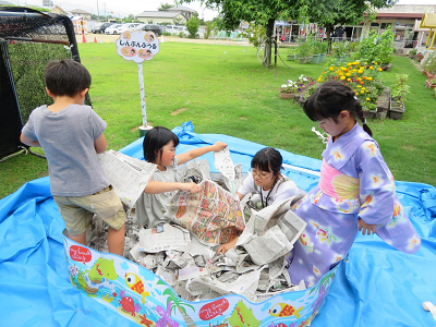 ビリビリに破いた新聞紙が入ったビニールプールの中に園児たちが入って遊んでいる写真