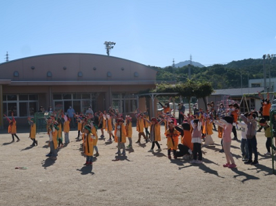 園庭で黄色い法被を着た園児たちが手を広げてポーズを取っている写真