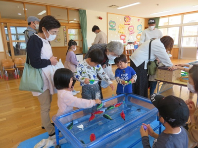 園児たちが保護者の方と水槽で魚釣り遊びを楽しんでいる様子の写真