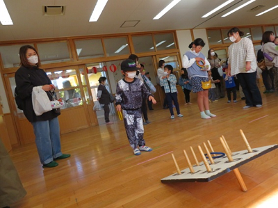 保護者の方が見守る中、一人の男の子が輪投げ遊びをしている写真