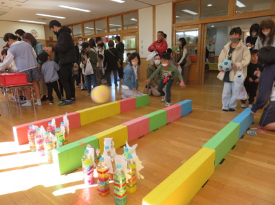 ペットボトルにカラフルなビニールテープが巻かれた手作りのボウリングのピンめがけて元気にボールを投げる男の子の写真