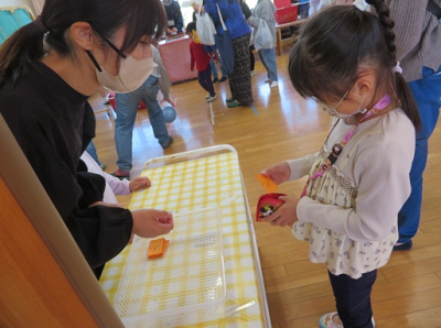 マスクを付けた女性にカウンター越しにオレンジの件を渡そうとしている女の子の写真