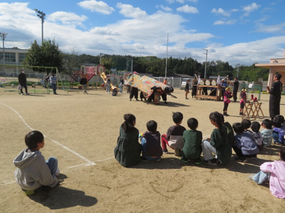 園庭で獅子のパフォーマンスを座って興味津々で眺めている子どもたちの写真