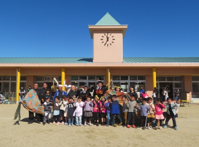 大きな時計のある昇降口の前で獅子といっしょに集合写真を取っている園児たちの写真