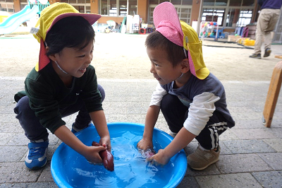 2人の男の子が青い桶でさつまいもを笑顔で洗っている写真