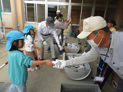 水色の帽子を被った女の子がおじさんにアルミホイルで包んださつまいもを手渡している写真