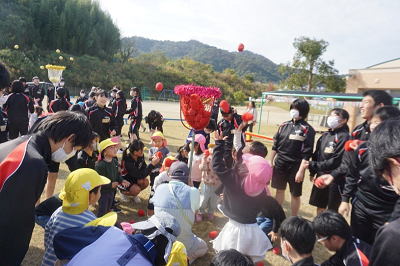 園庭で土煙を上げながら赤い玉をかごに入れている園児たちの写真