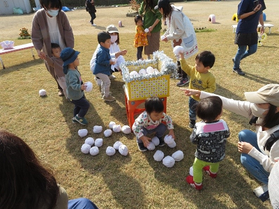 芝生の広場に設置された黄色いかごに白いボールを入れている園児たちの写真