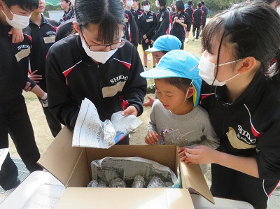 ジャージ姿の中学生の女の子2人と一人の男の子が段ボールに入った焼き芋を選んでいる写真