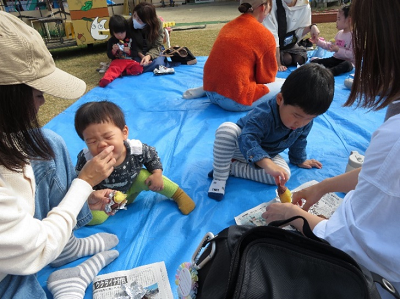 ブルーシートに座った保護屋と一緒に焼き芋を頬張っている園児2人の写真