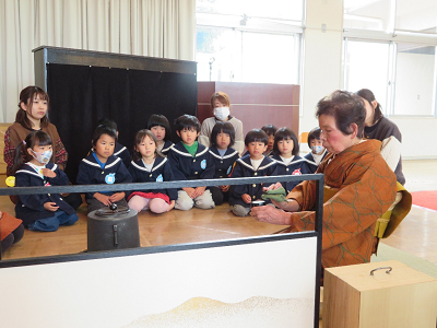 先生がお点前を披露し園児たちが興味津々で見学している様子の写真