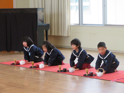 園児がお茶の道具の入ったお盆の前で正座してお茶の作法を学んでいる様子の写真