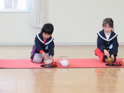 2人の園児が真剣な表情で茶碗を持ってお茶を点てている様子の写真