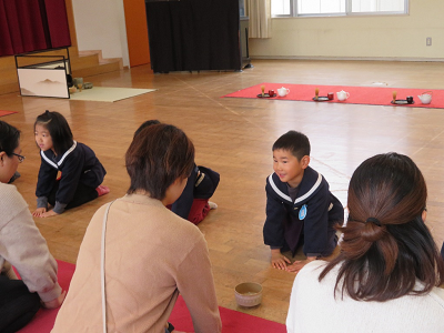 園児と保護者が向かい合うように正座で座り、園児が両手を揃えて笑顔でお辞儀をしている写真