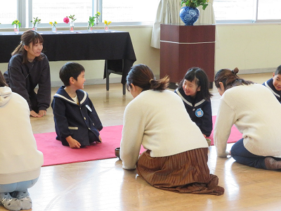 赤いカーペットに正座で座った園児たちと保護者らが向かい合って座り、互いにお辞儀をしている写真