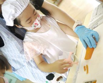 エプロン姿の子どもが先生に支えられながらピーラーで人参を調理している写真