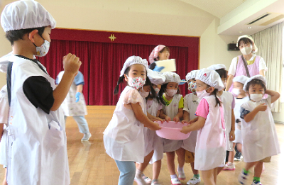 調理帽姿の子どもたちがみんなで大きなボウルを運んでいる写真