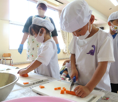 まな板の上でにんじんを真剣な表情で切っている子どもたちの写真
