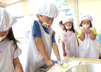 大きな包丁で玉ねぎを切る子どもとその様子を見守る友だちの写真